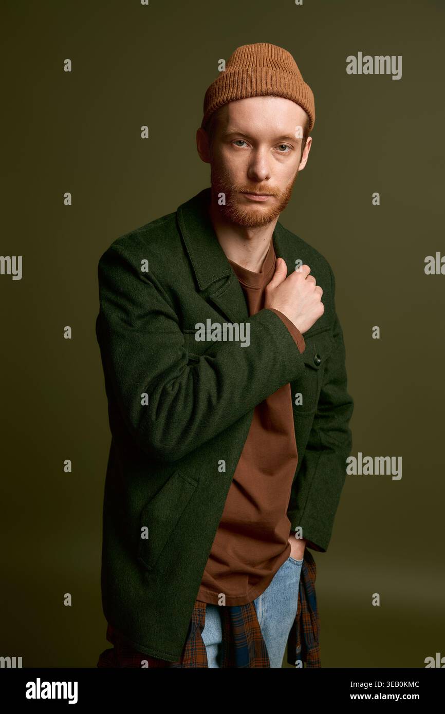 Handsome young man poses confidently in stylish attire against a muted ...