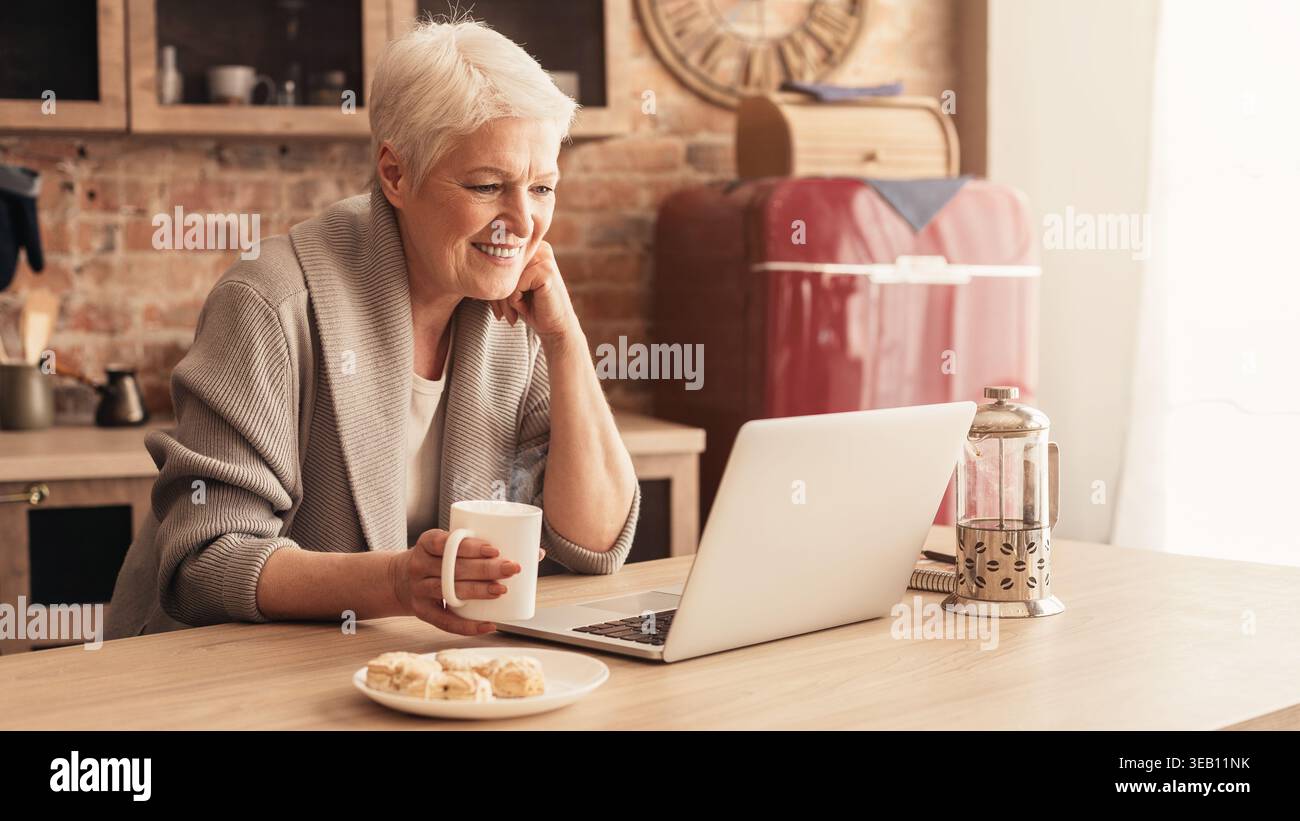 Woman Enjoying Cookies and Coffee While Using Laptop in Cozy Kitchen Setup Stock Photo