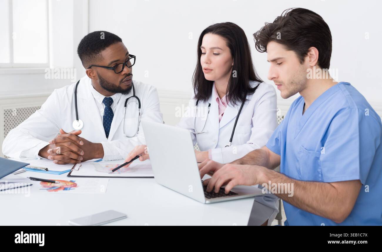 Young medical team discussing reports, using laptop Stock Photo