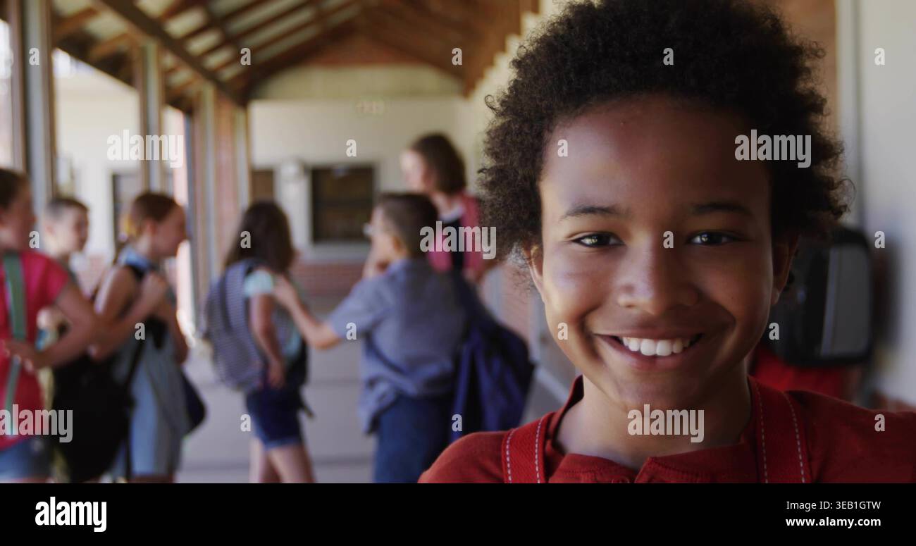 Smiling boy in red top wearing backpack straps standing in school corridor, with brick wall Stock Photo