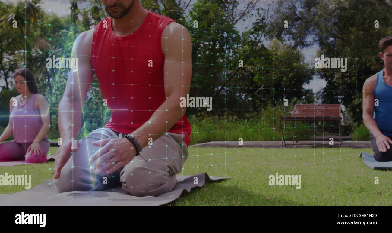 Kneeling man in red sleeveless top meditating on gray mat in park, showing bracelet and grid Stock Photo