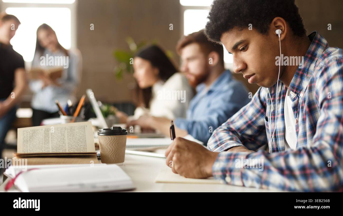 African-american guy preparing for exam, taking notes in library Stock Photo