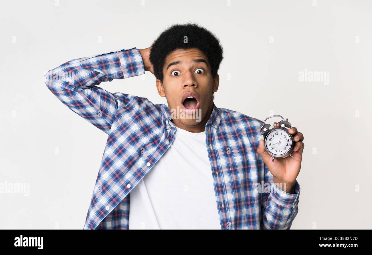 Shocked guy holding alarm clock over light background Stock Photo