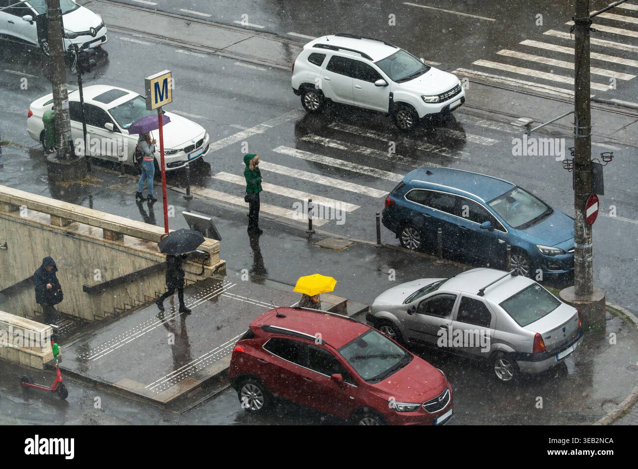 People stand under umbrellas on a busy street in the rain. Cars wait ...
