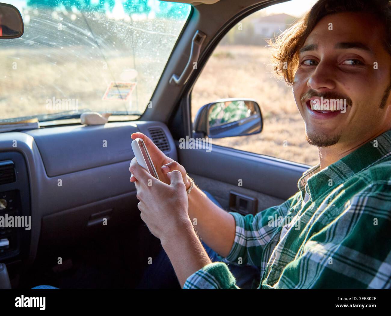 Smiling man using phone while driving car Stock Photo