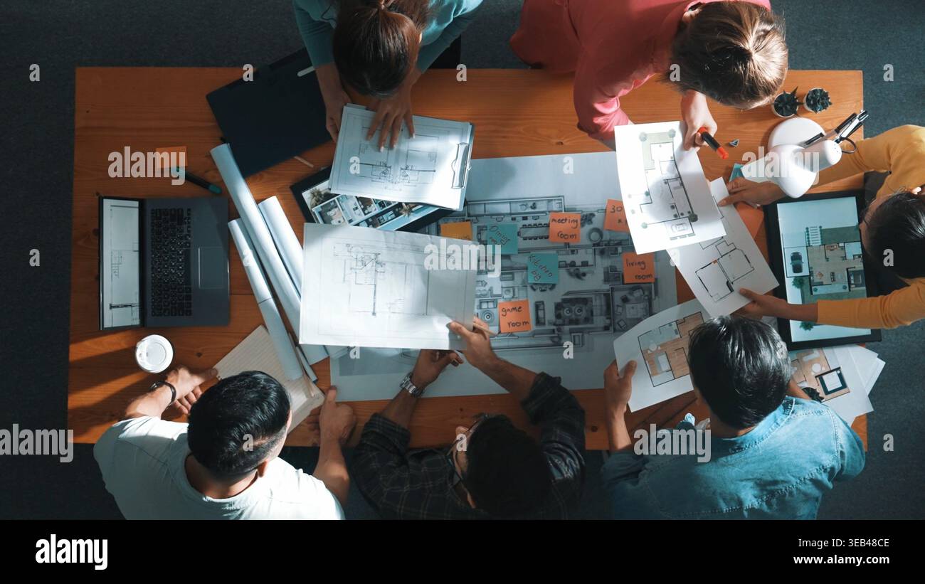 Top view of civil engineer team holding blueprint and standing at table with laptop, project plan and blueprint. Aerial view of skilled project Stock Photo