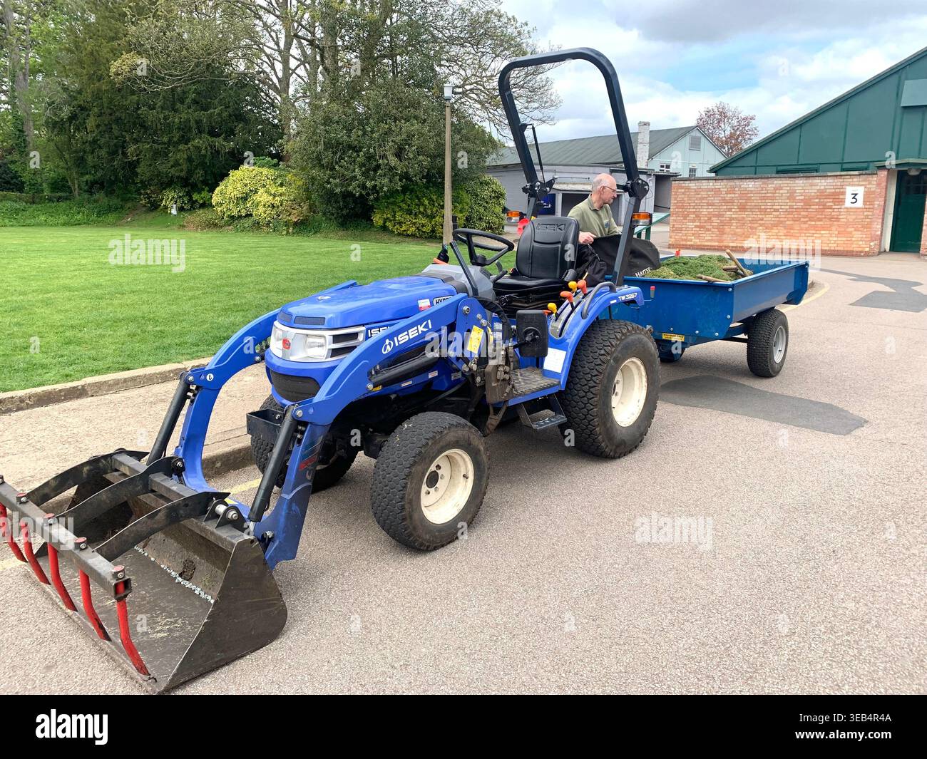 Grounds maintenance at Bletchley Park a worker operating a blue Iseki compact tractor with front loader during routine maintenanc - Smartphone Captured Stock Image