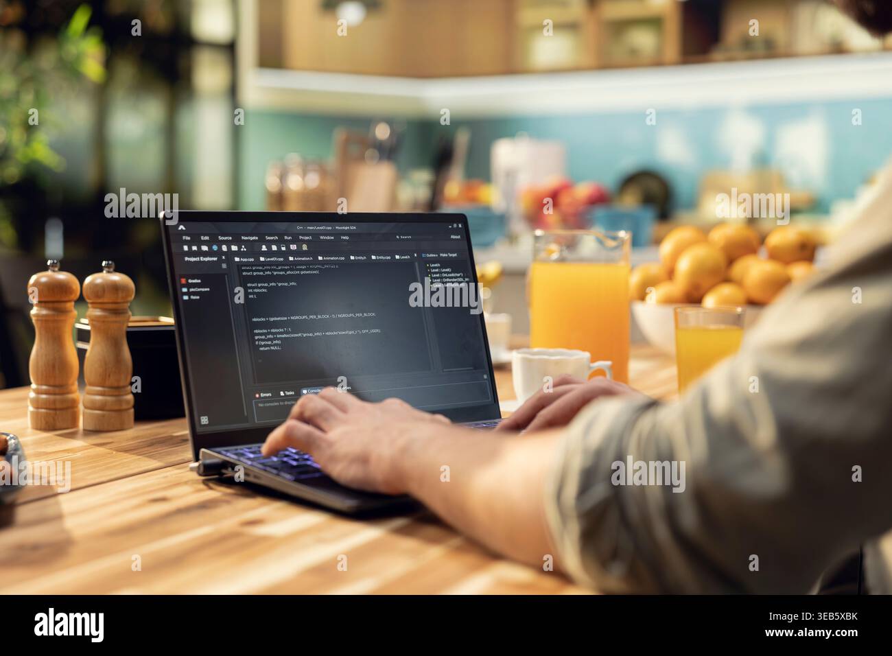 One person coding on laptop in a kitchen representing remote work in IT and software development. Programmer writes source code and uses command-line tools, highlighting engineering at home. Stock Photo