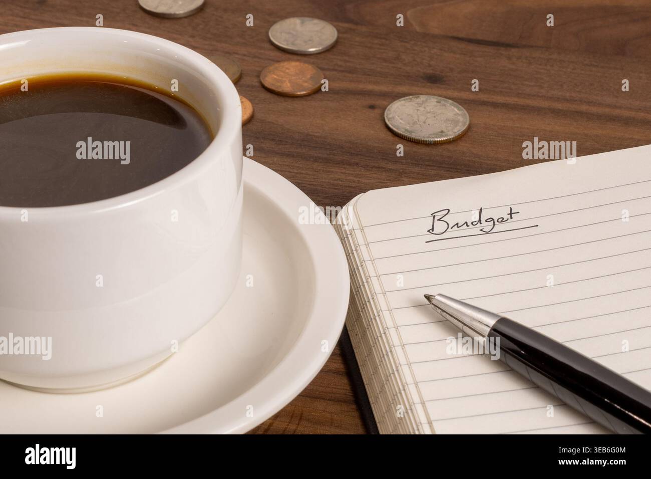 Open Notebook with “Budget” Written on Page, Coins and Coffee – Personal Finance Concept Stock Photo