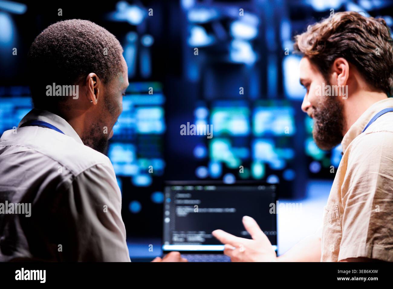IT developer collaborating with coworker in data center, crafting script code on laptop terminals. Proficient programmers engaging in maintenance work, ensuring optimal functionality and efficiency Stock Photo
