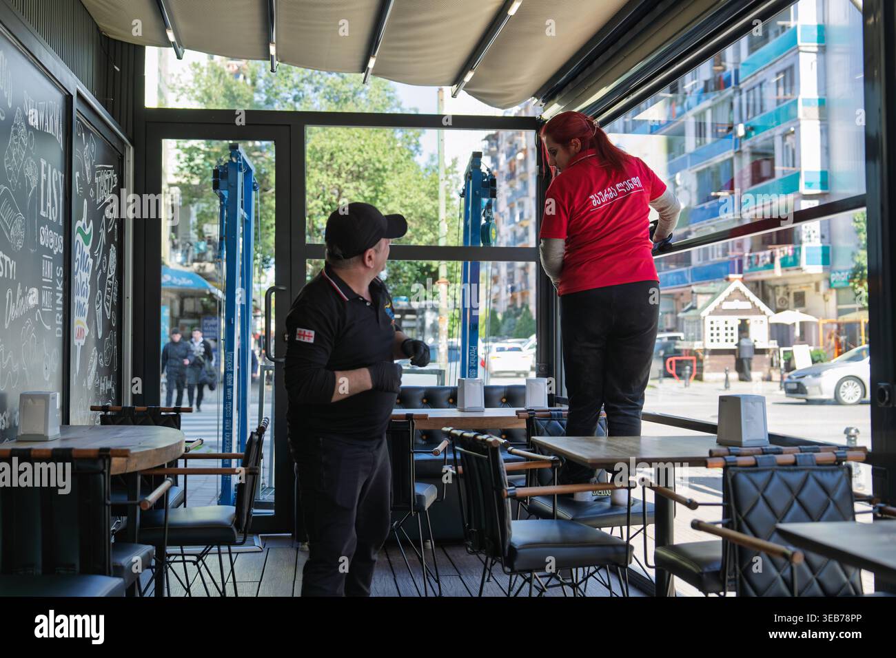 Batumi, georgia 21 april 2026: restaurant staff in batumi cleaning windows and tables inside a bright cafe, preparing for daytime service and welcomin Stock Photo