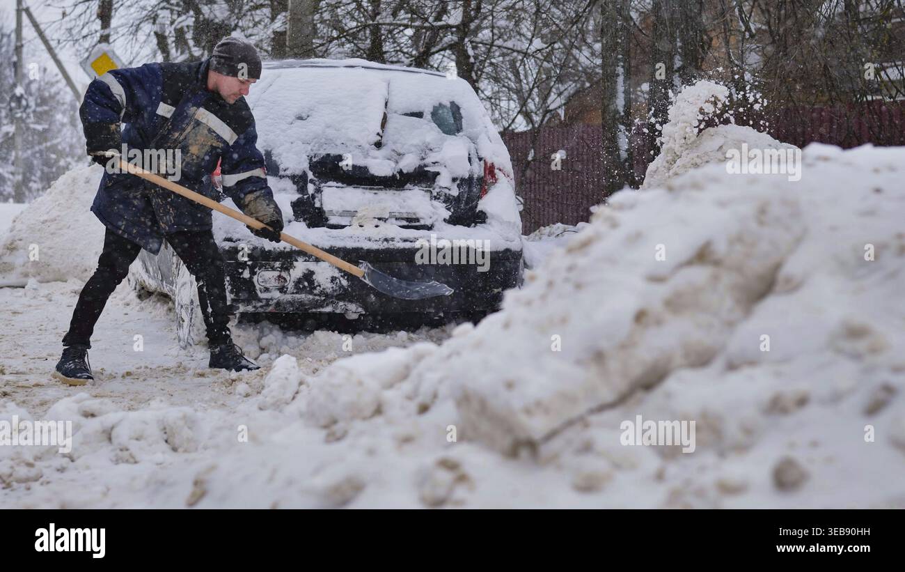 Man shoveling deep snow from car during harsh winter blizzard aftermath Stock Photo
