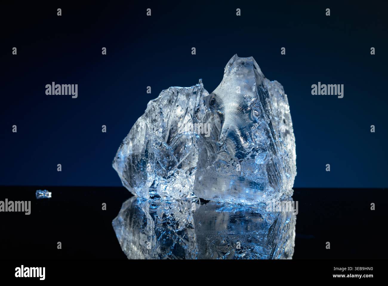 Broken ice with blue backlight on a black reflective background. Copy space. Stock Photo