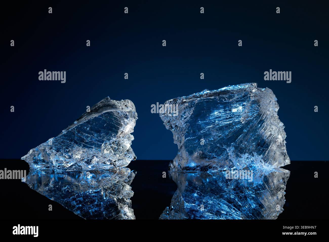 Broken ice with blue backlight on a black reflective background. Copy space. Stock Photo