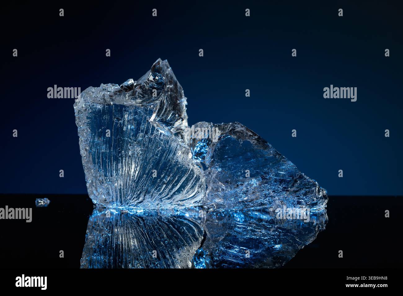 Broken ice with blue backlight on a black reflective background. Copy space. Stock Photo