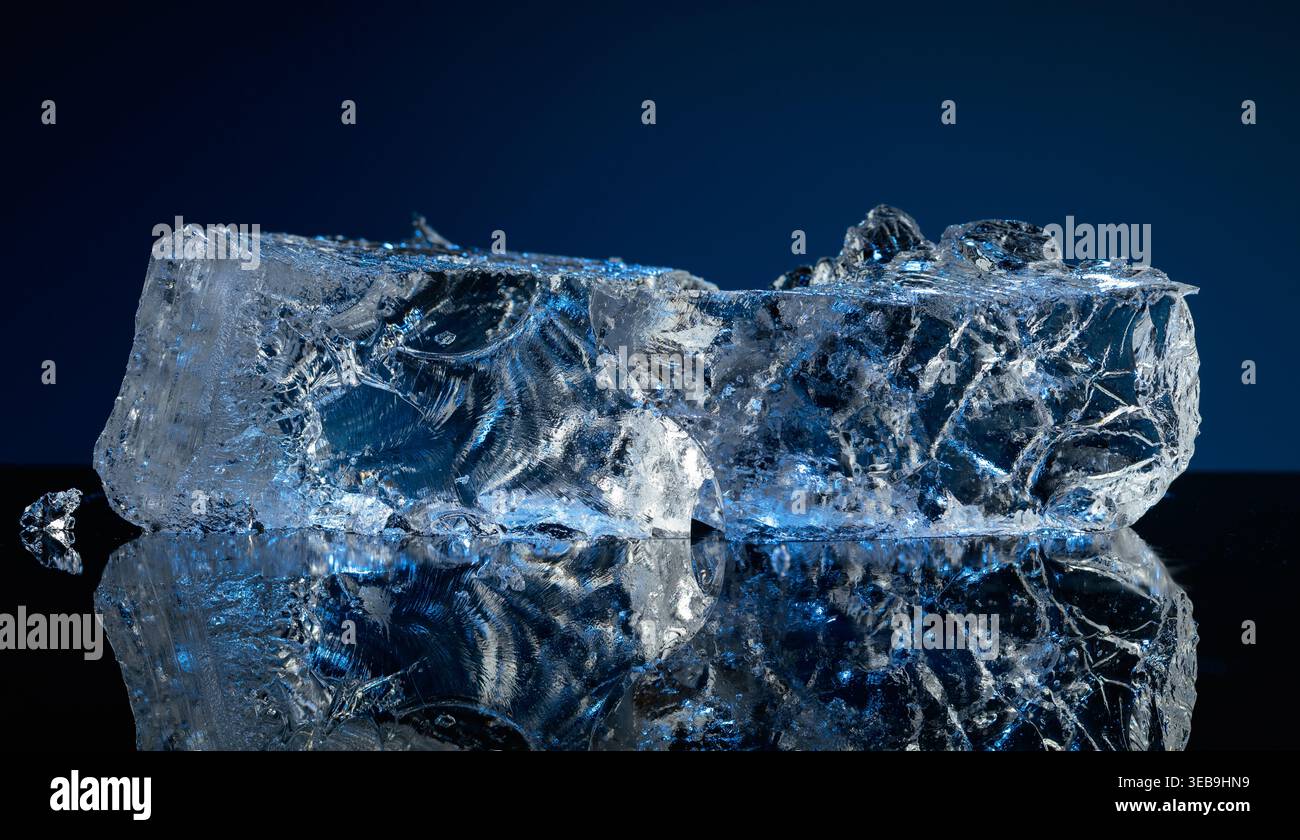Broken ice with blue backlight on a black reflective background. Copy space. Stock Photo