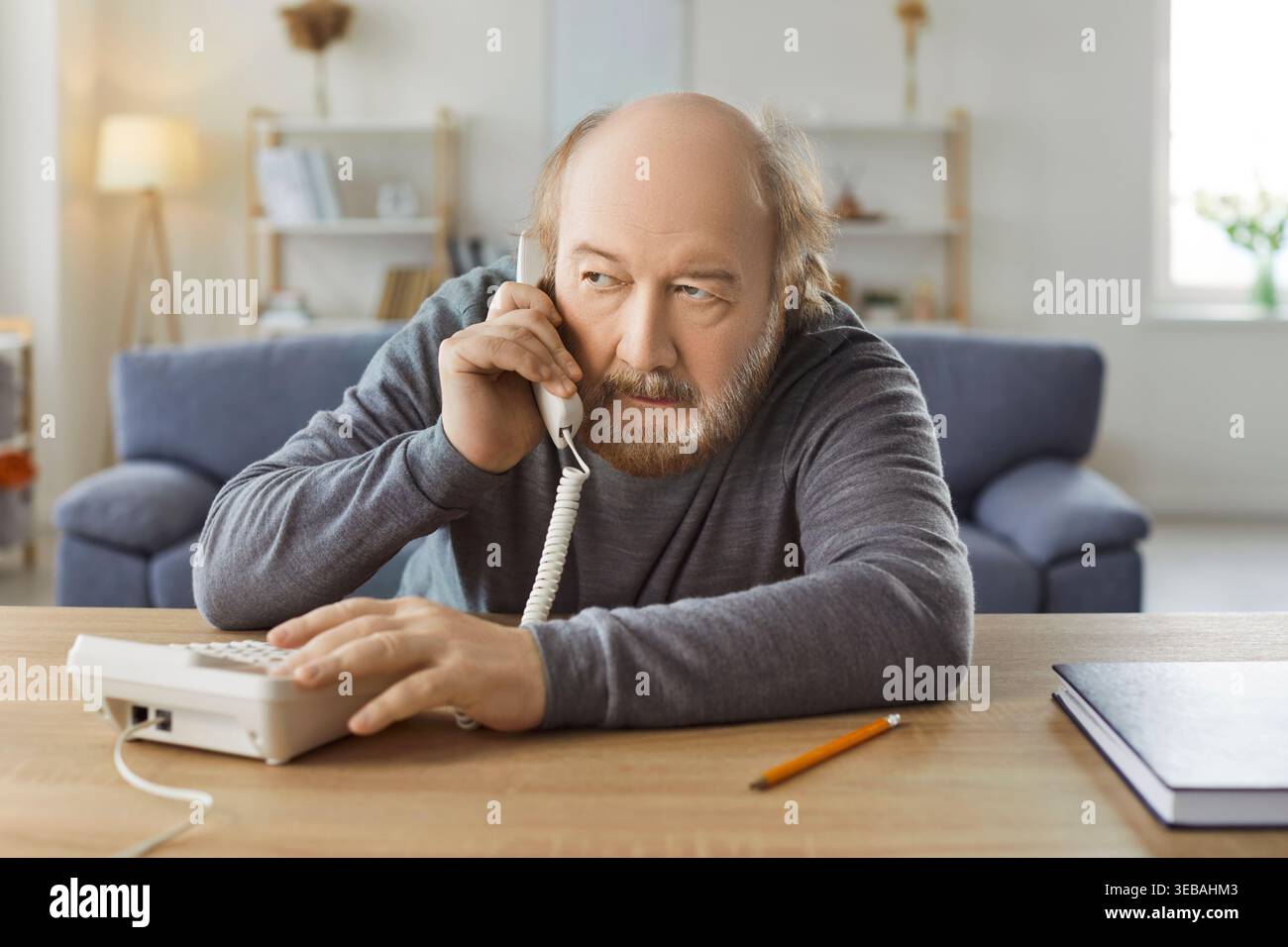 Serious Senior Man Talking On Phone Call At Home Stock Photo
