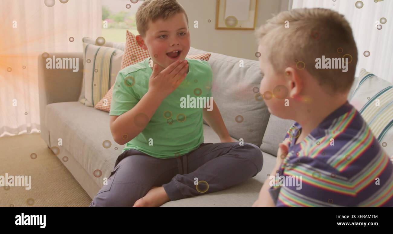 Talking two boys sitting on gray sofa in living room with patterned pillows, wearing green T-shirt Stock Photo