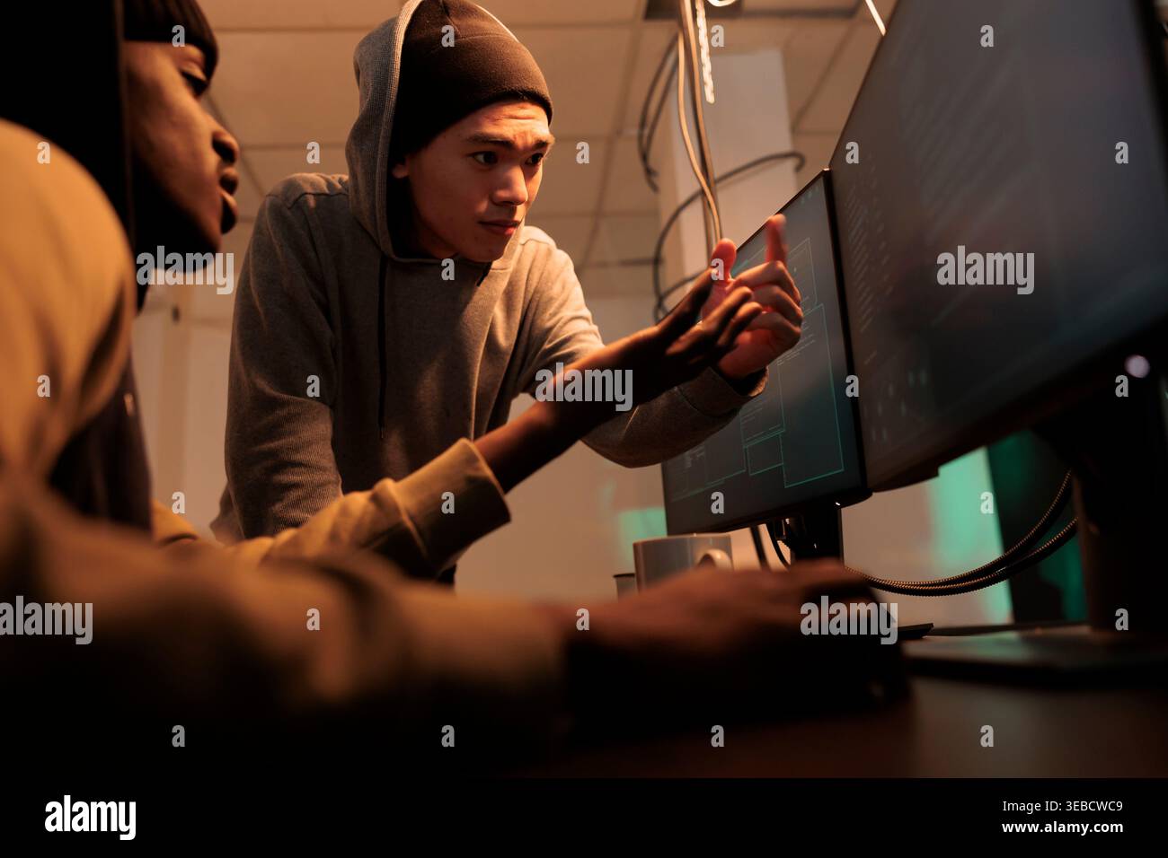 Internet criminals discussing computer system hacking, cyberattack. Hackers in hoodies coding password cracking pogram, scammers programming malicious software at night time Stock Photo