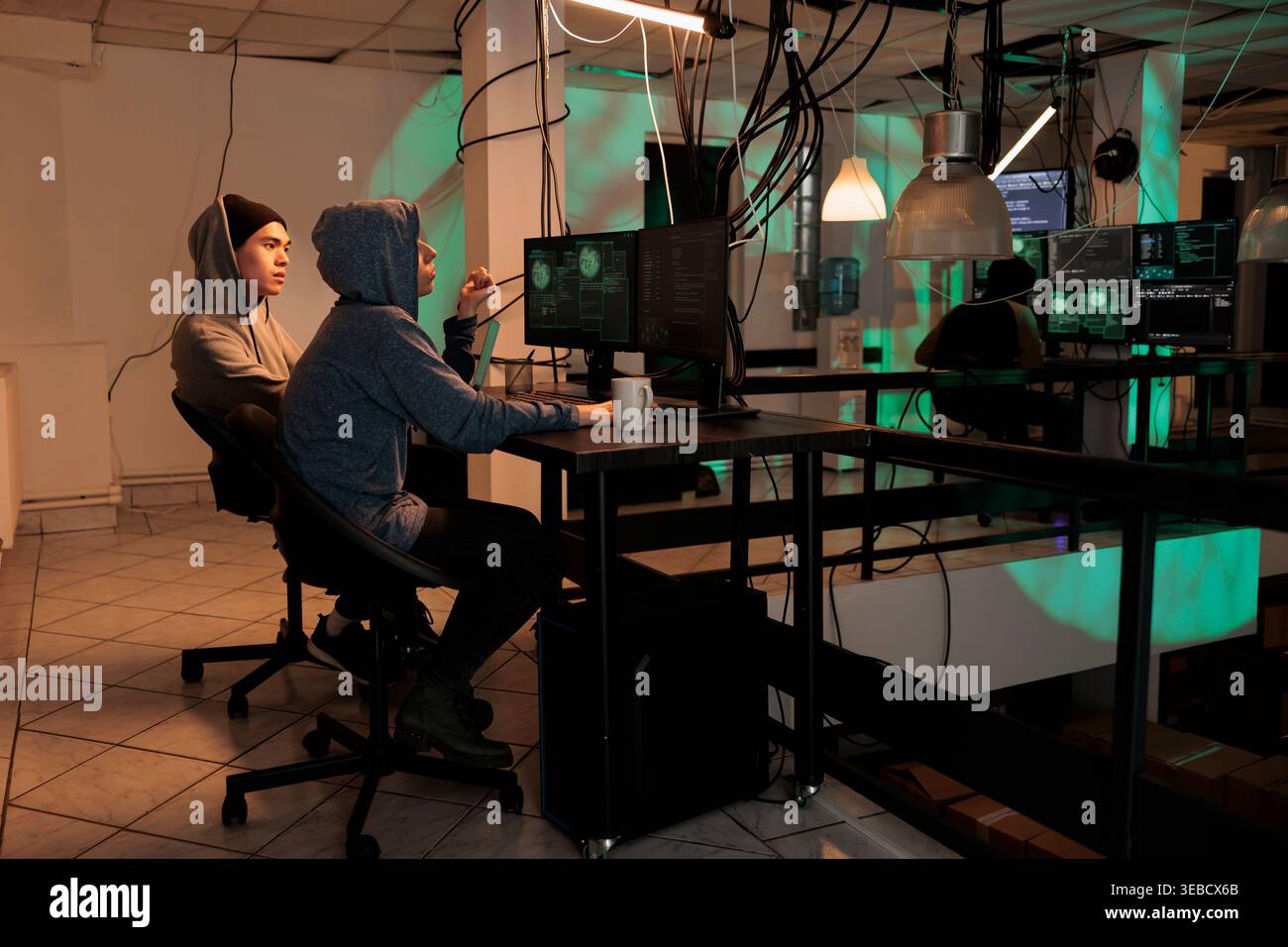 Cybercrime, internet thieves hacking computer system, stealing finances, coding malicious software. Hackers in hoods cracking password, programming internet virus at night time Stock Photo