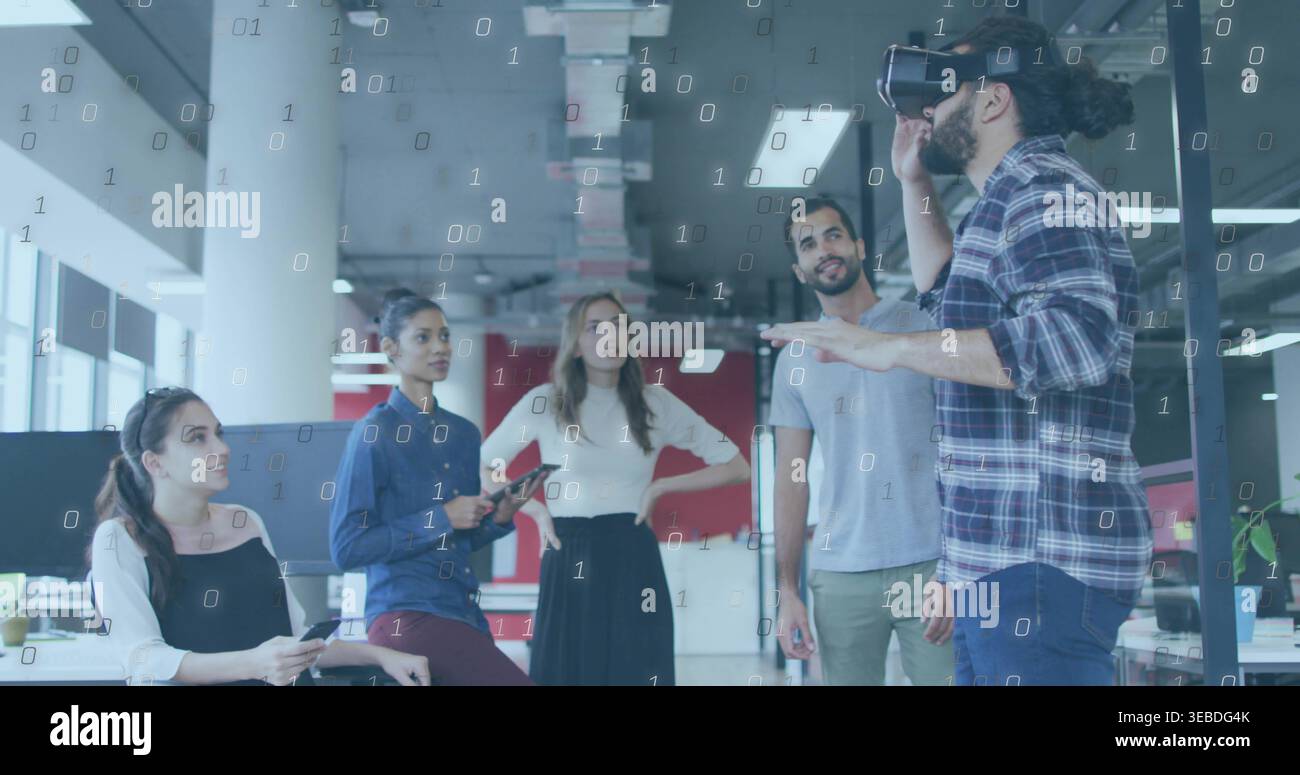 Demonstrating man wearing VR headset gesturing in modern office, with tablet, phone, binary overlay Stock Photo