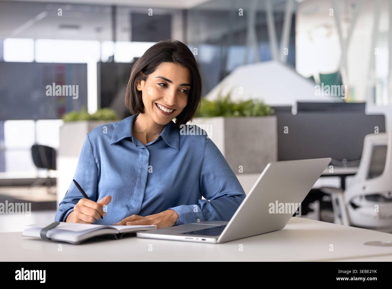 Woman watching educational content on laptop, making notes in notebook Stock Photo