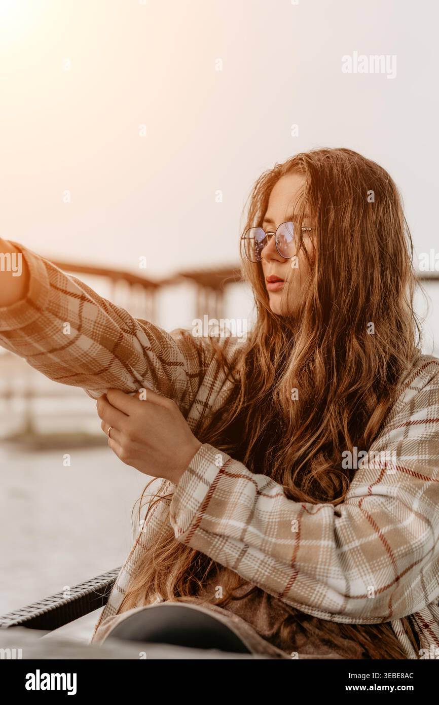 Woman plaid jacket eyeglasses adjusting her sleeve while sitting outdoors during a golden hour sunset Stock Photo