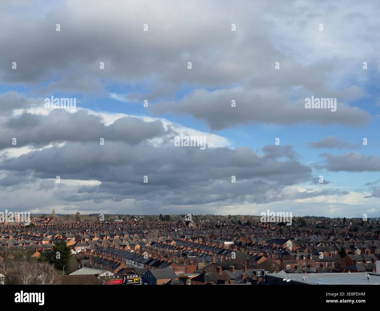 Suburban brick rooftops under dramatic layered clouds and blue sky Stock Photo