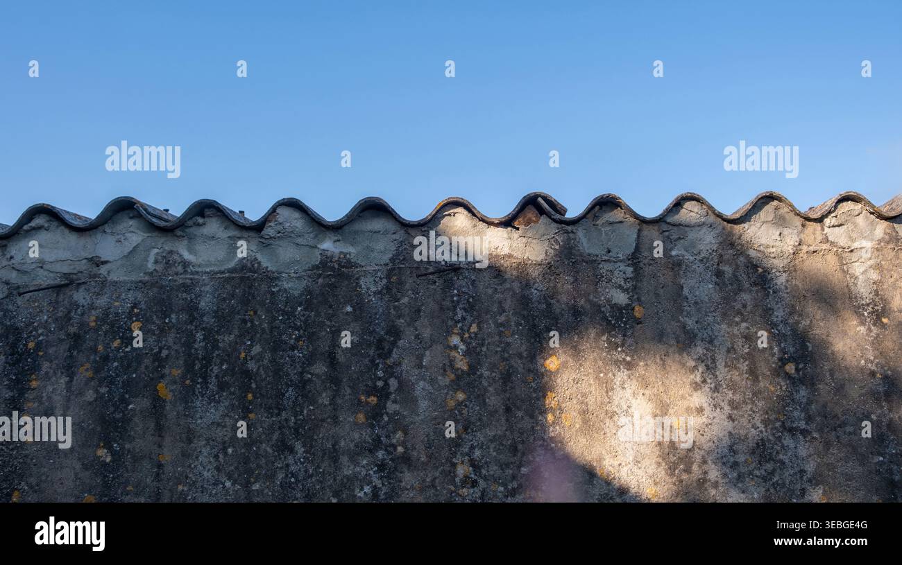 Old textured concrete wall with a wavy corrugated edge, closeup view. Blue sky background Stock Photo
