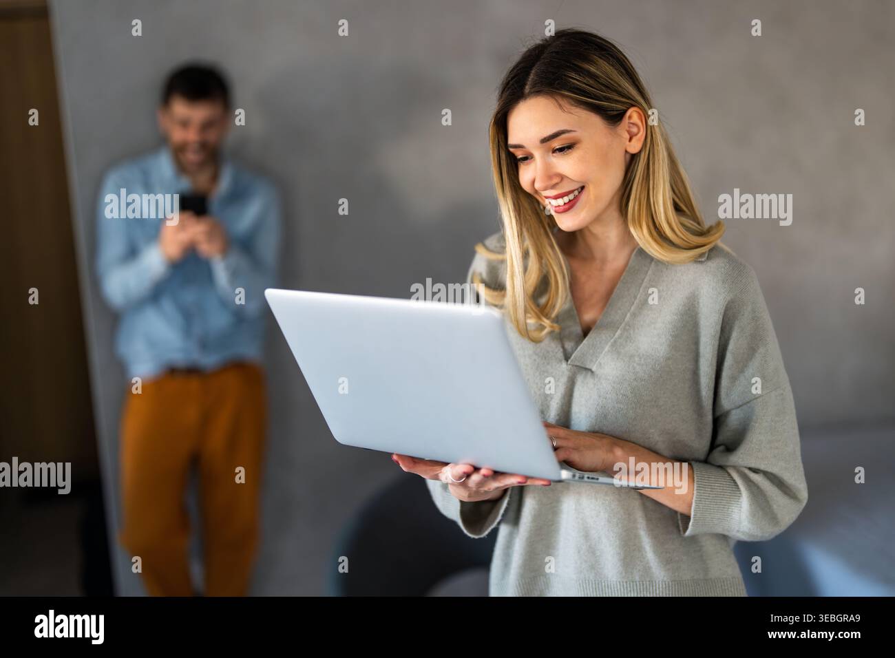 Young happy multiethnic couple having fun while using laptop, digital device at home Stock Photo