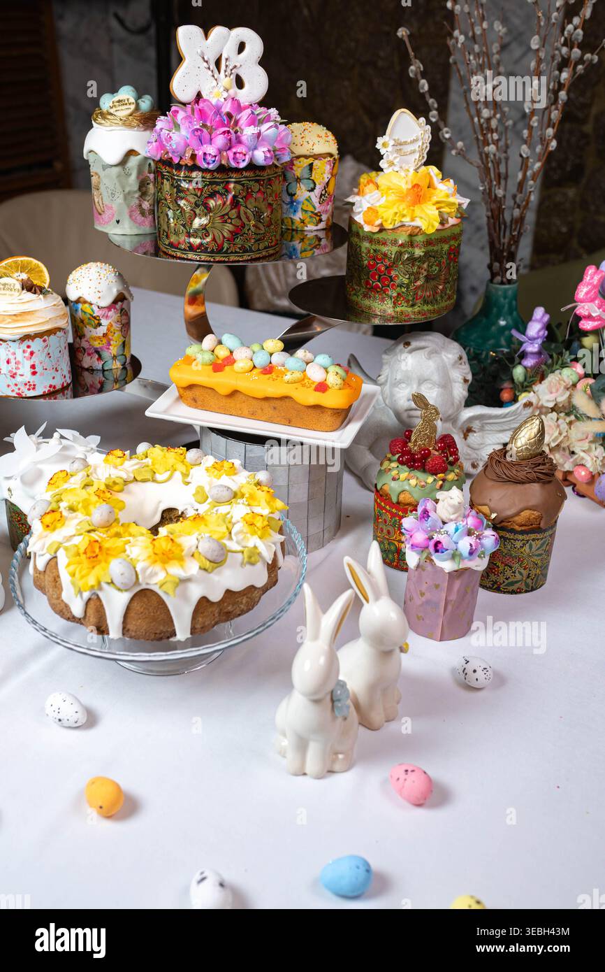 Vertical shot of ornate Easter cakes and ceramic bunnies on a white table. Stock Photo