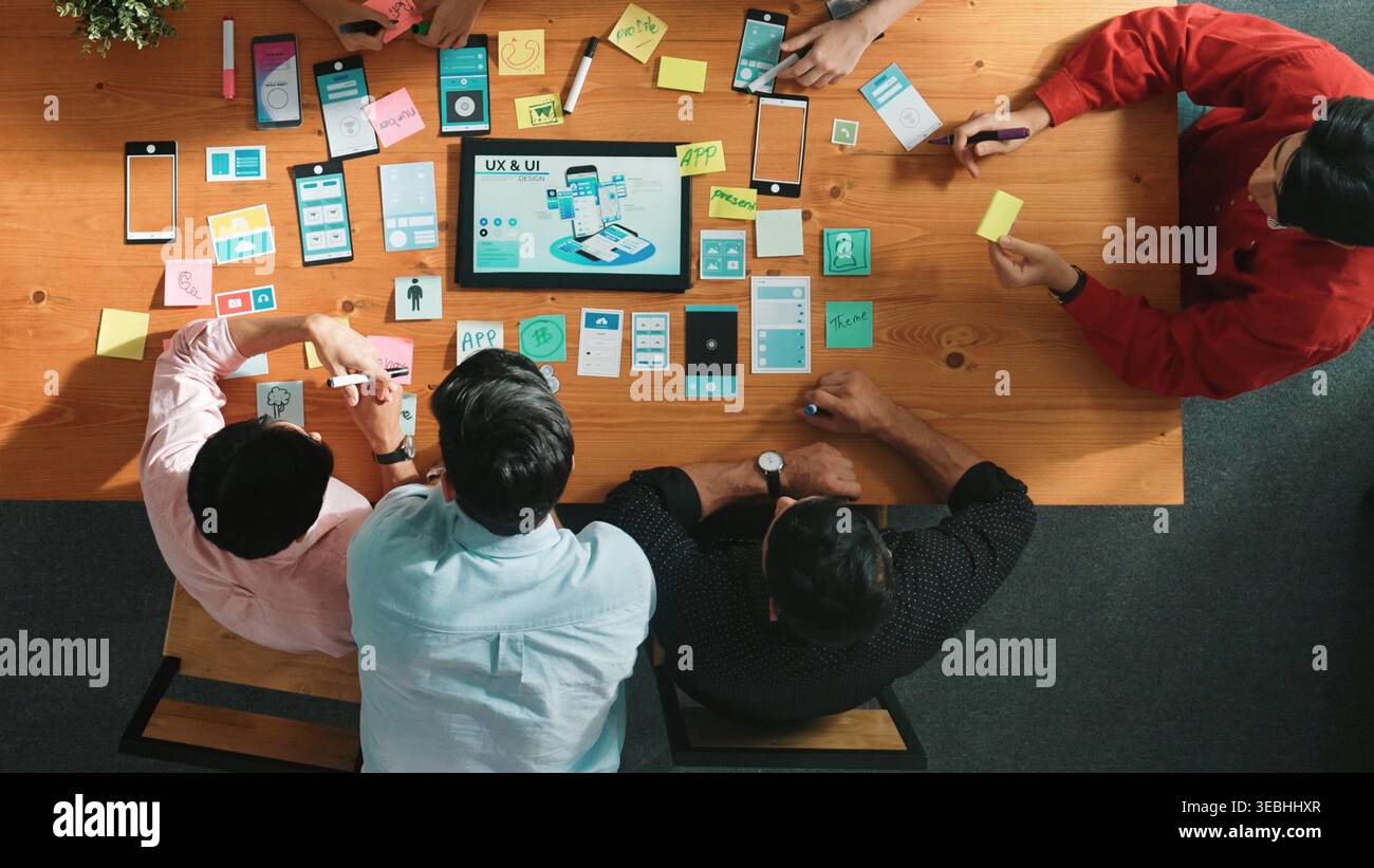 Programmer sharing Ux Ui design for mobile phone interface idea with software developer while designer writing idea at sticky notes. Start up team Stock Photo