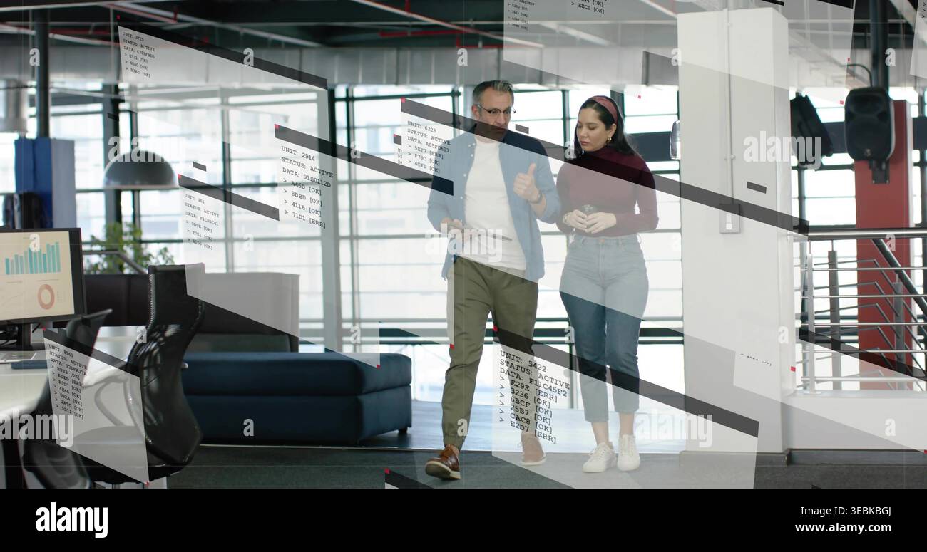 Walking pair discussing project in modern workspace, casually dressed with monitor charts on glass Stock Photo