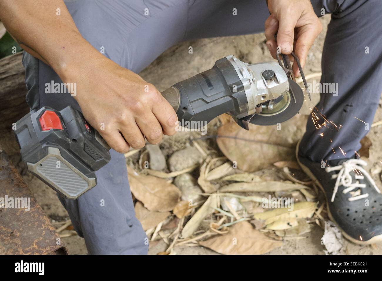 Focused worker holding cordless angle grinder tool with wrench adjusting cutting disc outdoors on ground covered with dry leaf preparing equipment for Stock Photo