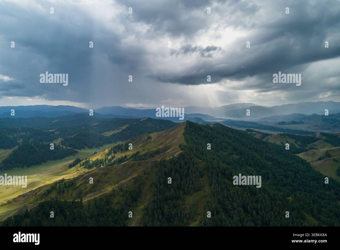 Altai Mountains landscape view with dark storm clouds and sun rays breaking through, illuminating green forest and valleys Stock Photo