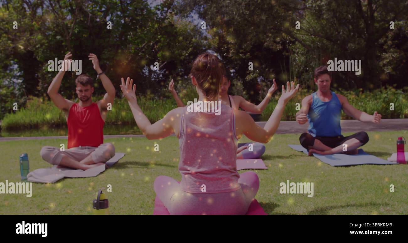 Leading instructor guiding group on yoga mats on park lawn wearing tank tops, with water bottles Stock Photo