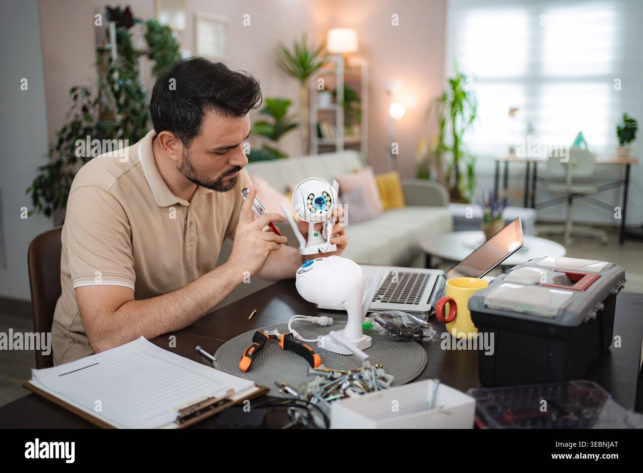 Man assembling a smart home security camera on a table with a laptop and tools Stock Photo