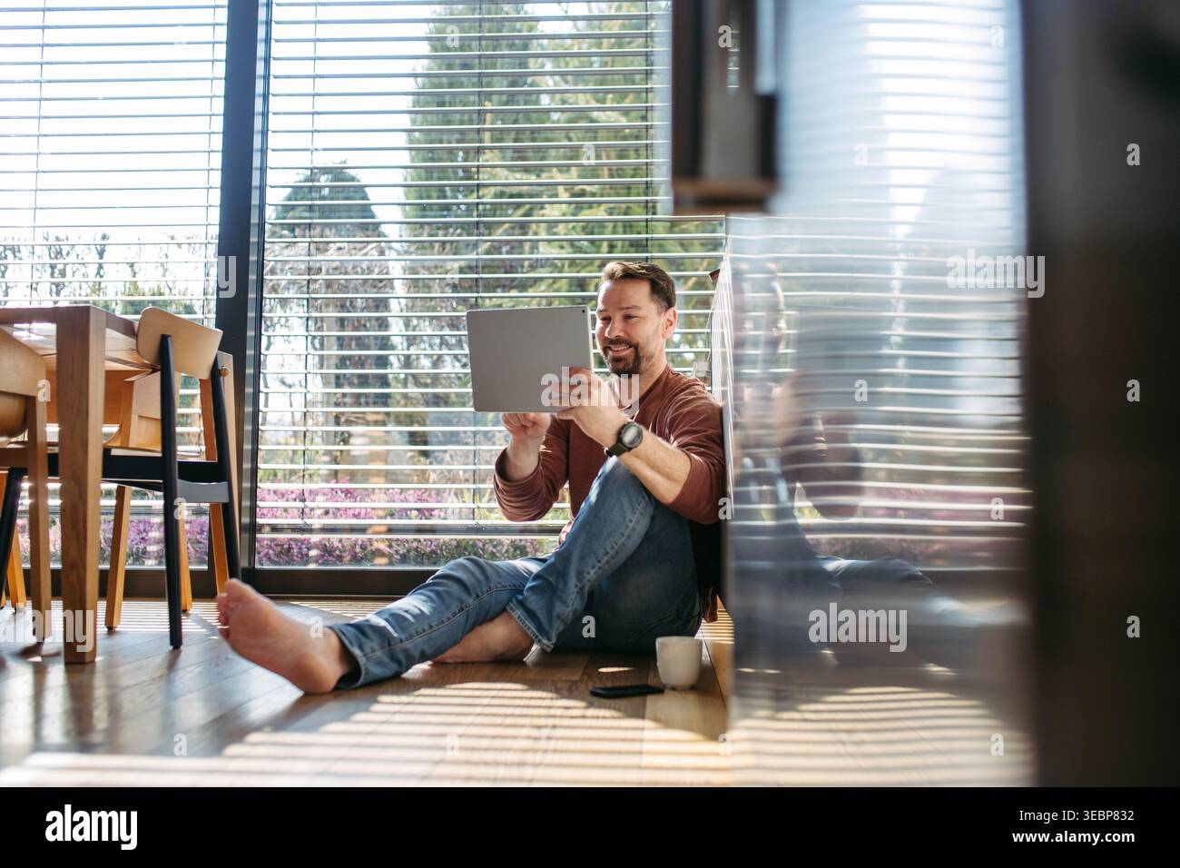 Man using smart home app working on tablet and sitting on floor. Stock Photo