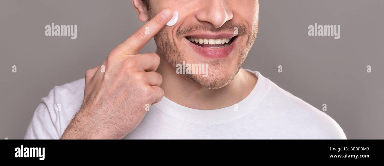 Smiling man moisturizing face with crea,. close up portrait Stock Photo