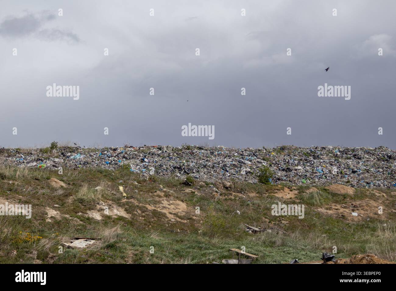 A large landfill is visible with various types of garbage piled up. The sky is grey with clouds above the site, indicating a possible rain in the area Stock Photo