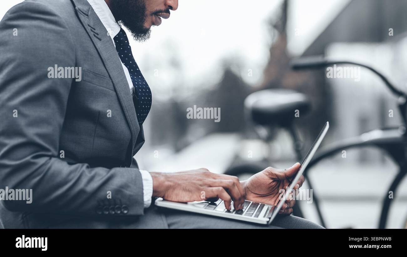 Man Works on Laptop While Sitting Outdoors Near Bicycle in Urban Area During Daytime Stock Photo