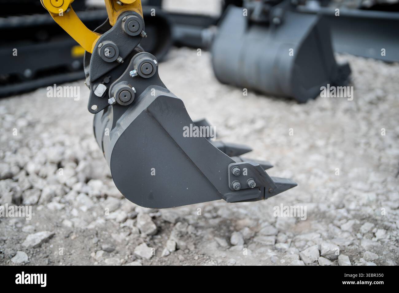 Heavy mini digger bucket suspended above gravel with tooth edge, side ...