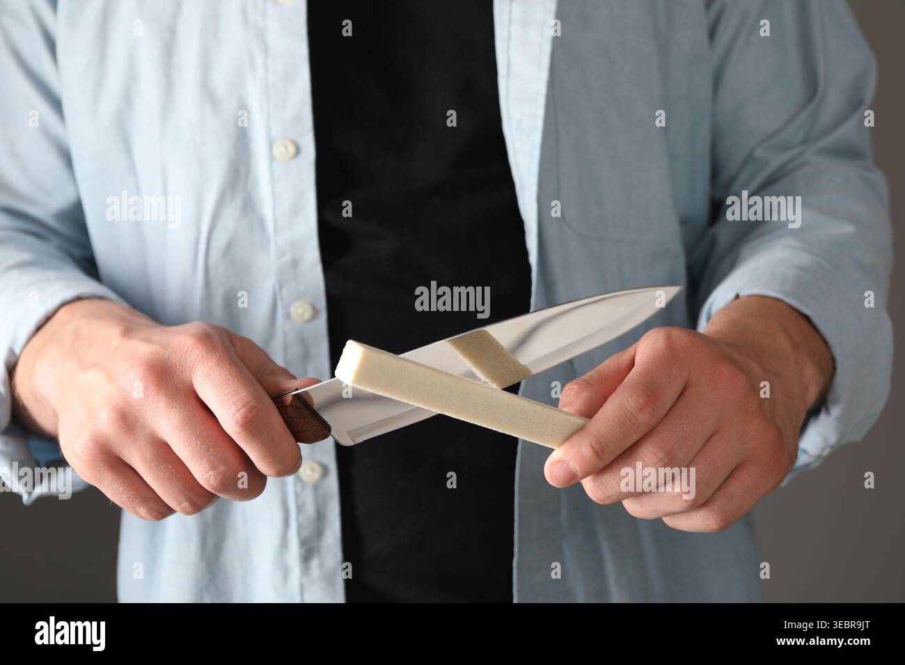 Man sharpening knife on grey background, closeup Stock Photo