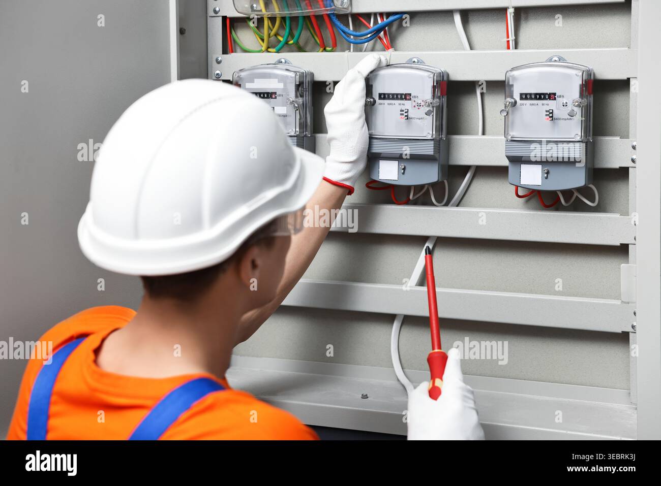 Electrician with screwdriver checking electrical meter indoors Stock Photo