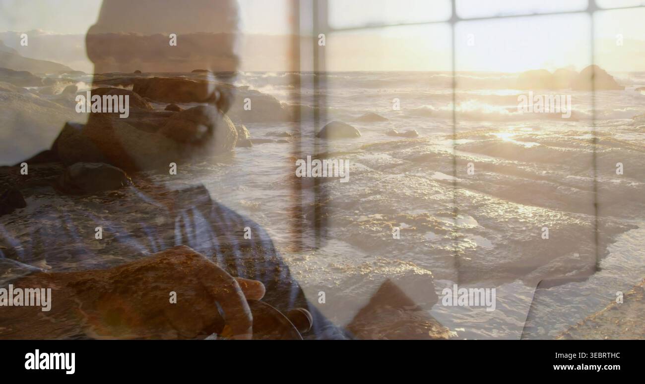Framing, man wearing glasses and blue striped shirt holding camera at seaside window panes, sunset Stock Photo