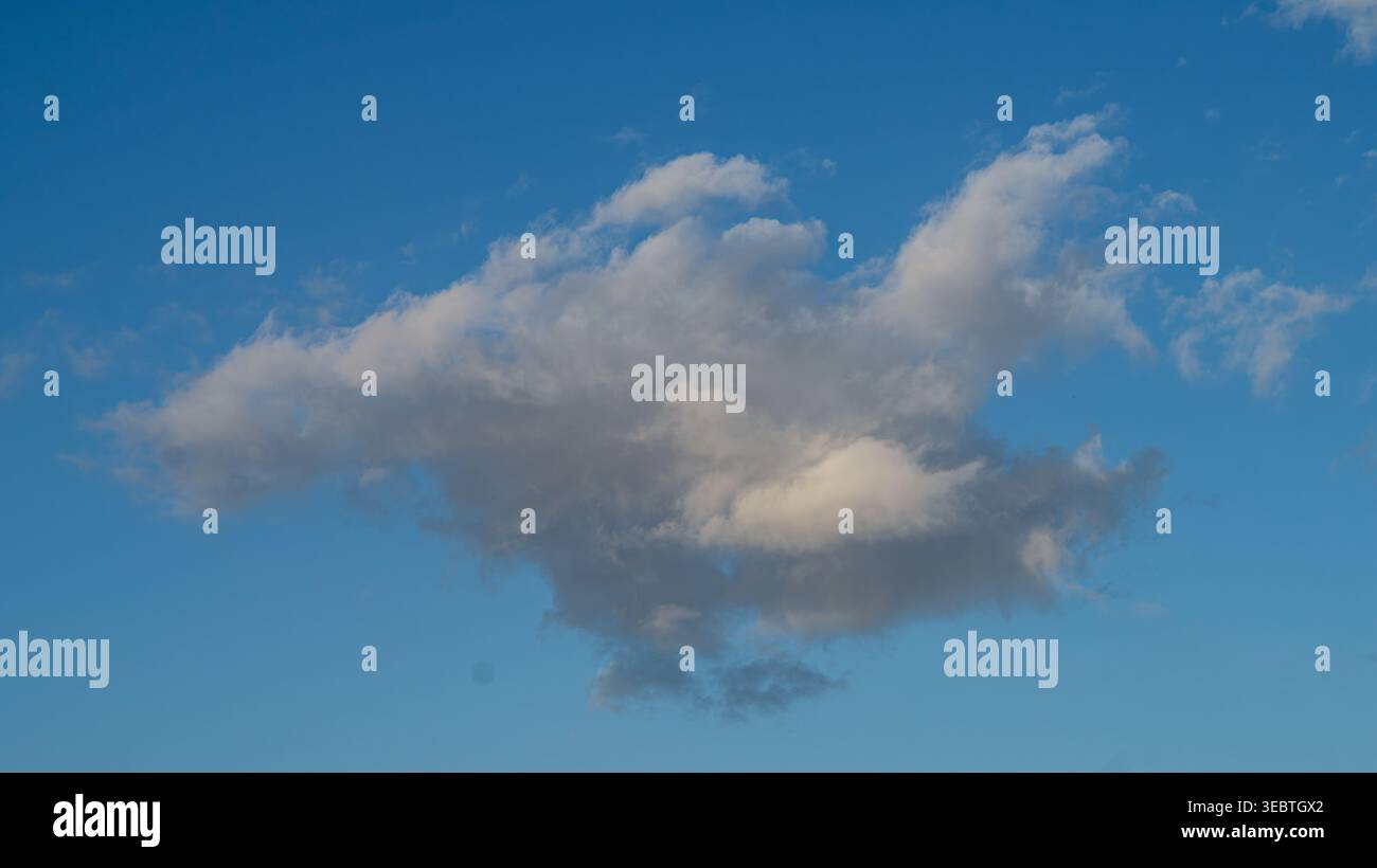 Single dramatic cumulus cloud against vivid blue sky, weather background Stock Photo
