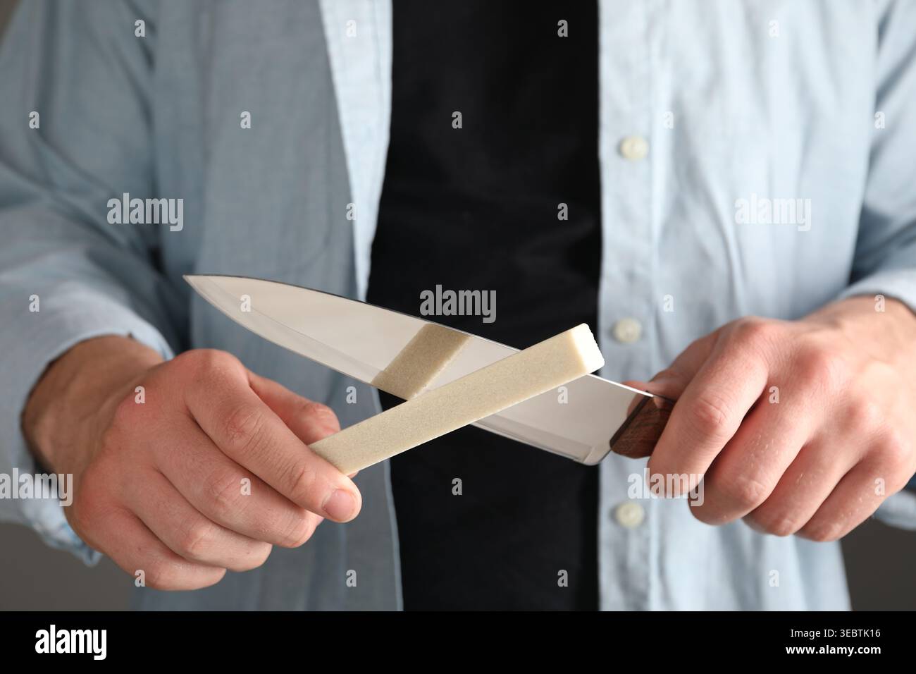 Man sharpening knife on grey background, closeup Stock Photo