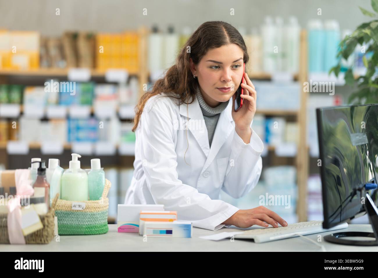 Female pharmacist working at computer and talking on phone Stock Photo