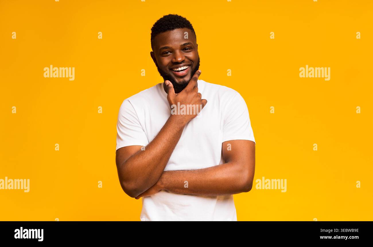 Man With Beard Smiles Joyfully Against a Bright Yellow Background While Posing Thoughtfully Stock Photo