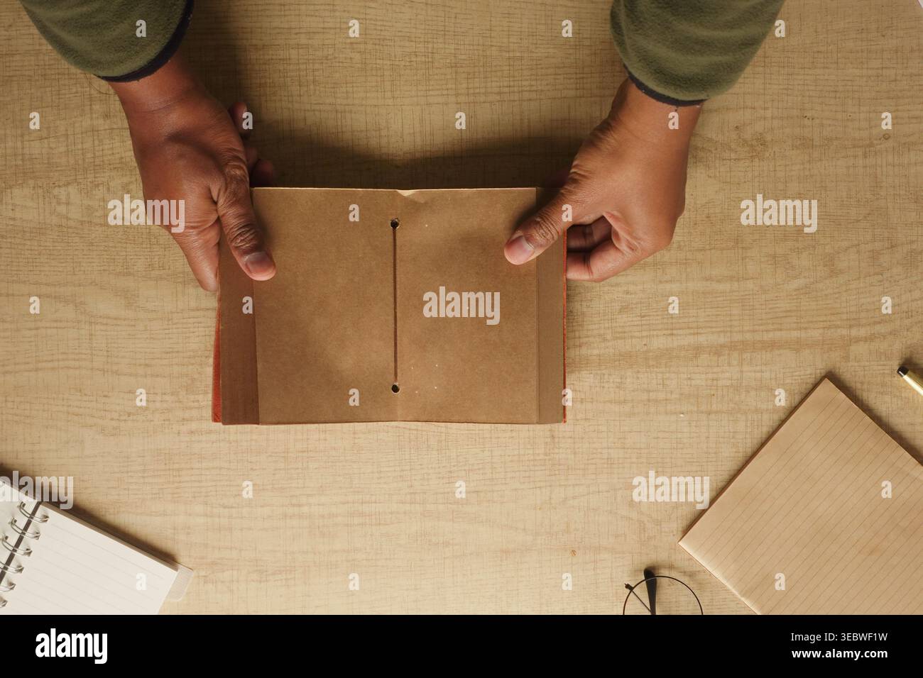 Hands hold a brown paper notebook on a wooden table Stock Photo